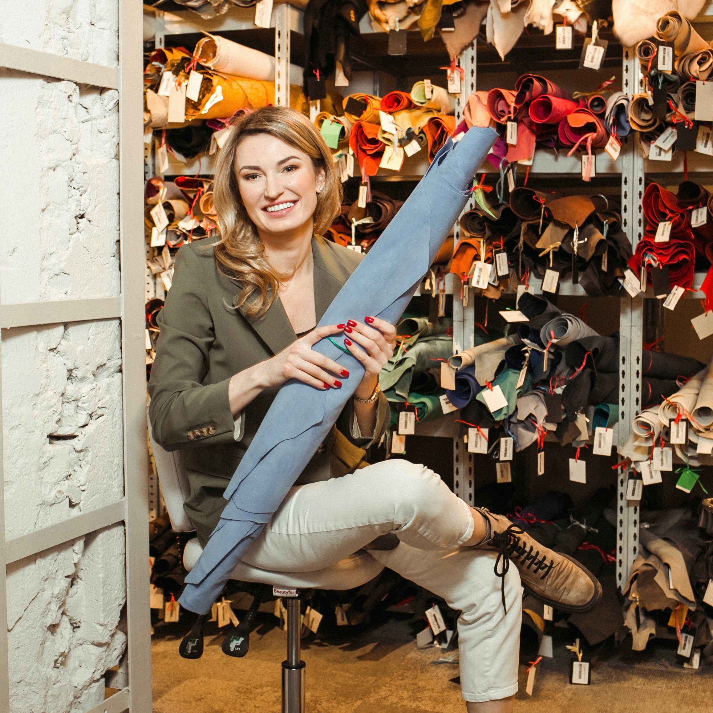 Young woman holding a roll of leather in blue color in front of leather stock
